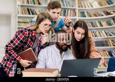 Junge Mixed-Race-Studenten oder Kollegen konzentrierten sich auf die Studie, das Projekt, die Zusammenarbeit im Lesesaal der Universitätsbibliothek mittels Laptop Stockfoto