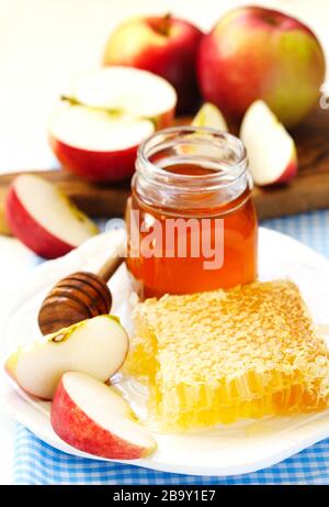 Waben mit Honig, Honig in Glasbecher und Scheiben reifer Äpfel auf Platte Stockfoto