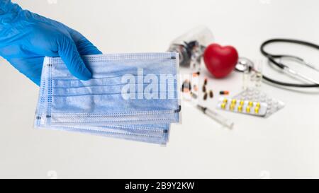 Hand, die eine medizinische Maske vor dem Hintergrund eines Stethoskops und der Pillen hält. Coronavirus Protection Konzept Stockfoto