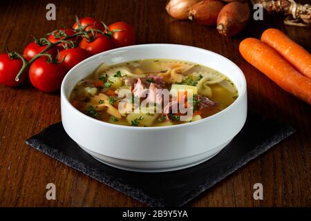 Suppe mit geräuchertem Fleisch, Gemüse und Pasta in einer weißen Schüssel Stockfoto