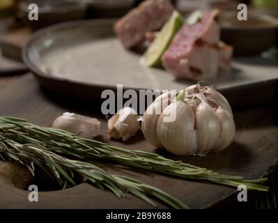 Rosmarin und Knoblauch, Zutaten liegen auf einer Schneideplatte auf einem Grund einer Platte mit Thunfisch-Steak und Kalk Stockfoto
