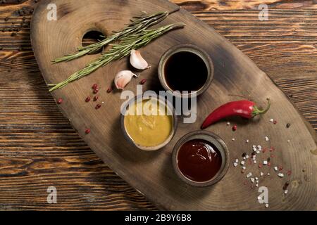 Zutaten, Knoblauch, Rosmarin, Chili, Tomaten- und Sojasoße, Senf, Gewürze, roter und schwarzer Pfeffer, Salz auf einem schönen dunklen Holzhintergrund, Stockfoto