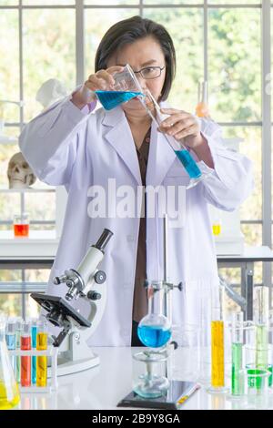 Entdecken Sie eine Heilung für eine asiatische Wissenschaftlerin, die konzentriert ist, halten Sie ein Reagenzglas und beobachten Sie während der Arbeit. Stockfoto