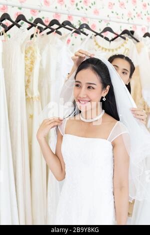 Eine asiatische Frau in einem weißen Hochzeitskleid versucht ihr nächstes Hochzeitskleid im passenden Raum. Stockfoto