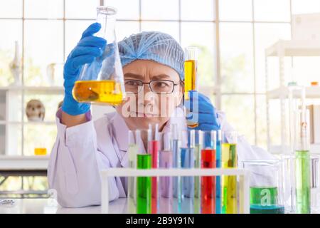 Entdecken Sie eine Heilung für eine asiatische Wissenschaftlerin, die konzentriert ist, halten Sie ein Reagenzglas und beobachten Sie während der Arbeit. Stockfoto