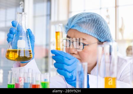 Entdecken Sie eine Heilung für eine asiatische Wissenschaftlerin, die konzentriert ist, halten Sie ein Reagenzglas und beobachten Sie während der Arbeit. Stockfoto