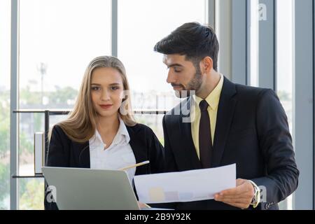 Zwei Geschäftsmänner und -Frauen waren sauber in eine Anzug- und Krawattenversammlung neben der Glaswand im Büro eingekleidet. Stockfoto