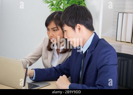 Zwei männliche und weibliche Asiaten halfen, einen Tisch voller Dokumente und Tablets, Notizbücher zu planen. Stockfoto