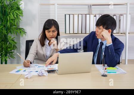 Zwei männliche und weibliche Asiaten halfen, einen Tisch voller Dokumente und Tablets, Notizbücher zu planen. Stockfoto