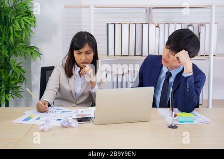 Zwei männliche und weibliche Asiaten halfen, einen Tisch voller Dokumente und Tablets, Notizbücher zu planen. Stockfoto