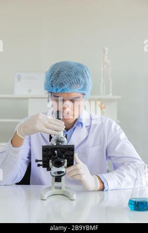 Junger Wissenschaftler mit Mikroskop im Labor. Forscher, die weißen Mantel am Schreibtisch tragen und Proben mit Mikroskop im Labor betrachten. Stockfoto