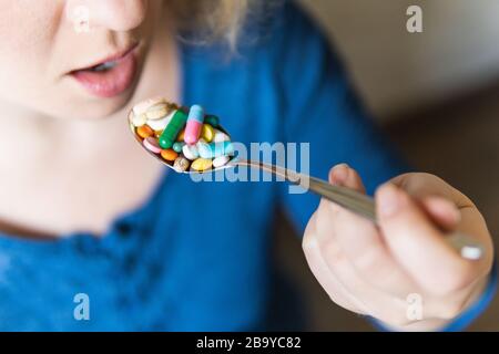 Junge blonde Frau, die einen vollen Löffel verschiedener Pillen vor ihrem offenen Mund hält. Stockfoto