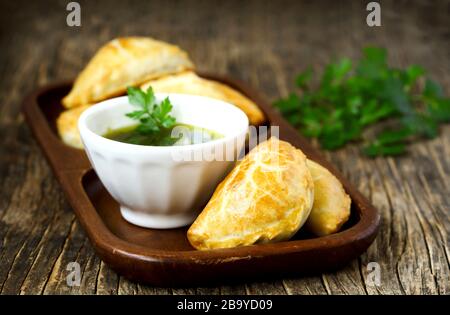 Empanadas mit Schimichurri auf Holztisch Stockfoto