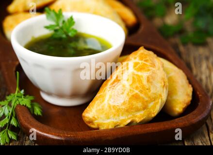 Empanadas mit Schimichurri auf Holztisch Stockfoto