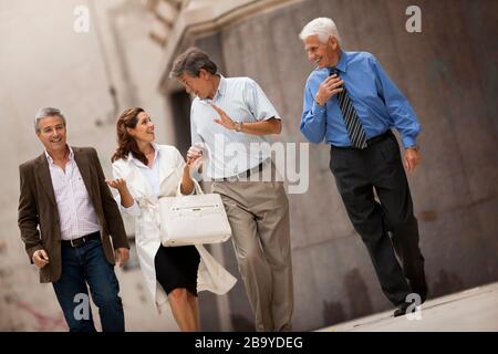 Drei Geschäftsleute und eine Kollegin sprechen und lachen, wenn sie auf einer Straße in der Stadt zusammen gehen. Stockfoto