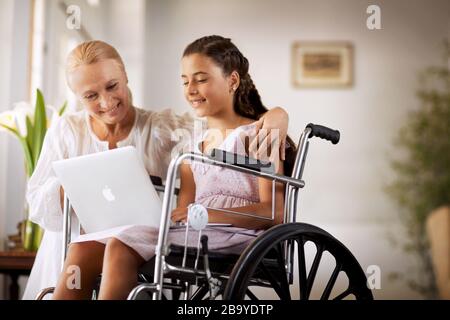 Junge Mädchen im Rollstuhl, etwas Übersicht zu ihrer Großmutter auf einem Laptop. Stockfoto