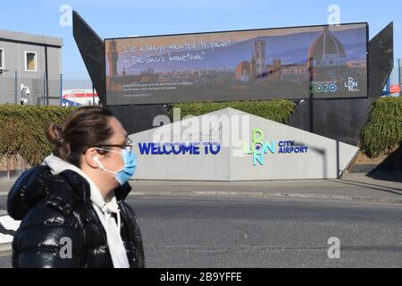 Eine Frau, die eine Gesichtsmaske trägt, spaziert durch den Flughafen London City, der seinen Betrieb bis Ende April einstellen wird, inmitten eines Zusammenbruchs der Nachfrage, der durch den Ausbruch des Coronavirus verursacht wurde. Stockfoto