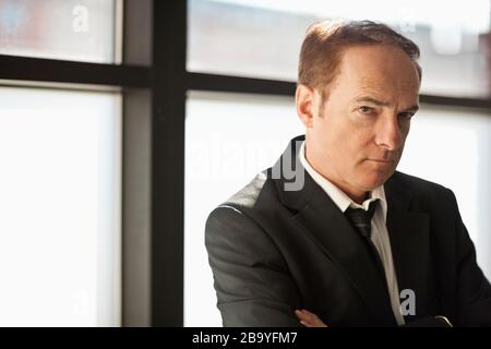 Geschäftsmann im Anzug steht mit umgeklappten Armen. Stockfoto