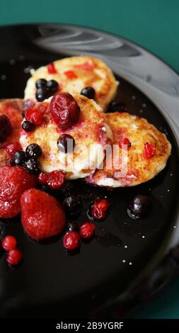 Käsekuchen mit Beeren auf schwarzem Teller. Vertikales Foto Stockfoto