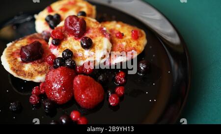 Käsekuchen mit Beeren auf schwarzem Teller und grünem Hintergrund Stockfoto