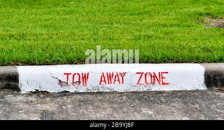 Wegschleppen Zonenschild in roten Buchstaben auf einer Bordsteinkante auf einer Durchfahrt mit grünem, beschnittenen Rasen dahinter. Stockfoto