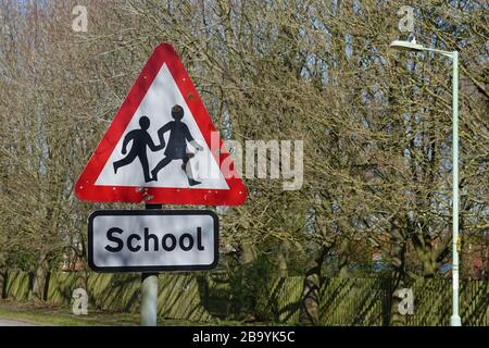 Martlesham Heath, Suffolk - 25. März 2020: Vorsicht Kinder überfahren. Rotes Warndreieck Straßenschild in der Nähe einer Schule. Schulen für Coronavirus. Stockfoto