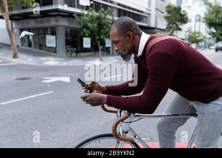 Afroamerikanischer Mann sitzt auf seinem Fahrrad und benutzt sein Telefon Stockfoto