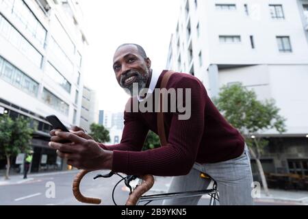 Afroamerikanischer Mann sitzt auf seinem Fahrrad und benutzt sein Telefon Stockfoto