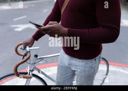 Afroamerikanischer Mann hält sein Fahrrad und sein Telefon in der Straße der Stadt Stockfoto