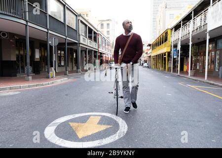 Afroamerikanischer Mann, der neben seinem Fahrrad in der Straße der Stadt spazieren ging Stockfoto