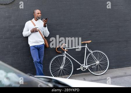 Afroamerikanischer Mann mit einem Telefonanruf und seinem Fahrrad auf der Straße Stockfoto