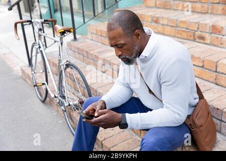 Afroamerikanischer Mann, der auf einer Treppe sitzt und sein Telefon benutzt Stockfoto