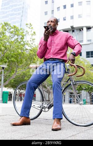 Afroamerikanischer Mann sitzt auf seinem Fahrrad und benutzt sein Telefon Stockfoto