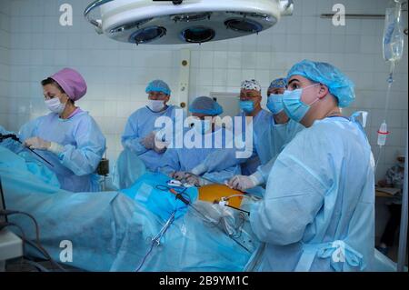Chirurgen in Gesichtsmasken, die um die Patientenplatte stehen und eine Operation durchführen, eine künstliche Beatmungsmaschine für die Lunge. Januar 2019. Kiew Stockfoto
