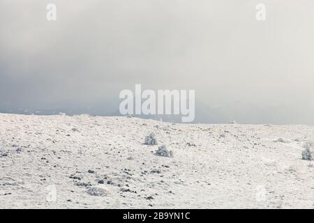 Schöne, abstrakte, sanfte Sicht auf schneebedeckte Berghochländer und entfernte felsige Gipfel kaum sichtbar durch den Nebel Stockfoto