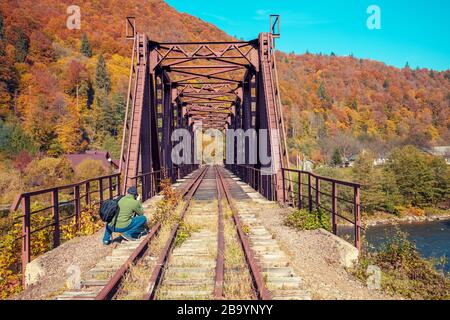 Alte Eisenbahn auf der Brücke über den Bergfluss im Herbst. Ein Mann macht sich ein Bild von der Eisenbahn Stockfoto