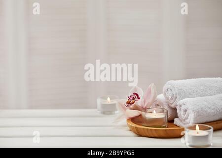 Spa-Zusammensetzung mit aromatischen Kerzen, Orchideenblume und Handtuch auf weißem Holztisch. Beauty-Spa-Behandlung. Kopierer Stockfoto