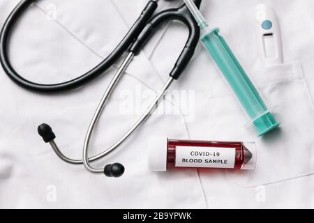 Draufsicht über medizinische Geräte und Reagenzgöhrchen mit einer mit Kovid 19 infizierten Blutprobe auf einem weißen Arztkleid, Gesundheits- und Medizinkonzept, selektiv Stockfoto