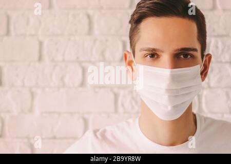 Porträt des müden jungen Mannes in weißer medizinischer Maske im Gesicht zum persönlichen Schutz während der Coronavirus COVID-19-Pandemie. Erschöpfter selbstbewusster Arzt WEA Stockfoto