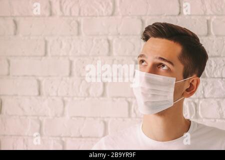 Portrait erschöpfter junger Mann, der eine Schutzmaske auf dem Gesicht trägt und nach oben auf den Kopienraum blickt. Müde nachdenkliche Ärztin in weißer medizinischer Gesichtsmaske. Persona Stockfoto