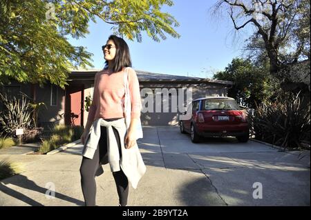 Asiatische Frau trägt einen rosa Pullover zu Fuß eine Auffahrt mit einer Tasche um die Schulter. Stockfoto