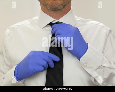 Ein Geschäftsmann passt eine schwarze Krawatte an, während er sterile blaue Nitrilgummihandschuhe und ein weißes Hemd in Nahaufnahme trägt. Stockfoto