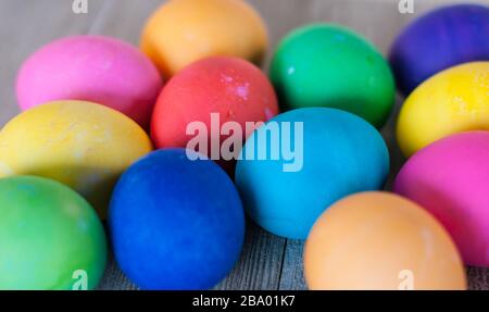 Nahaufnahme von 12 blau, rosa, rot, gelb, orange und grün gefärbten Eiern auf grauem verwittertem Holzhintergrund Stockfoto