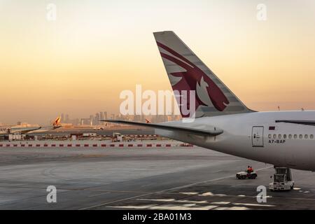 Der Schwanz eines Boeing-Flugzeugs der Qatar Airways 777 am Flughafen von Doha am frühen Morgen mit der Skyline der Stadt Stockfoto