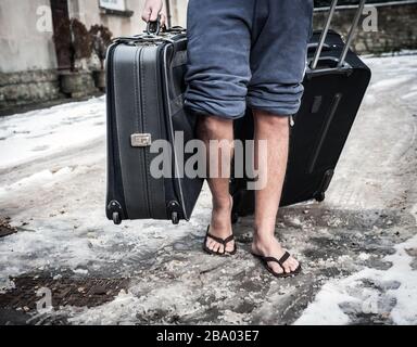 Mann, der mit Koffer im Winterschnee Flip-Flops trägt Stockfoto