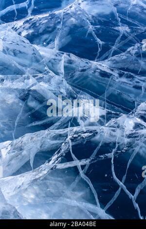 Natürliche Struktur von klarem blauem Eis mit tiefen Rissen. Schöne Risse im Klareis des Sees. Vertikal. Stockfoto