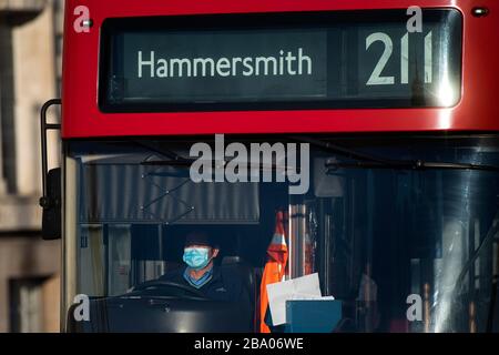 Ein Londoner Busfahrer, der eine Gesichtsmaske auf der Westminster Bridge, London, trug, nachdem Premierminister Boris Johnson die Entscheidung getroffen hatte, Großbritannien in einen Lockdown zu bringen, um die Ausbreitung des Coronavirus einzudämmen. Stockfoto