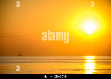 Segelboot in der Ferne unter der untergehenden Sonne in der Nähe von Santorini, Griechenland Stockfoto