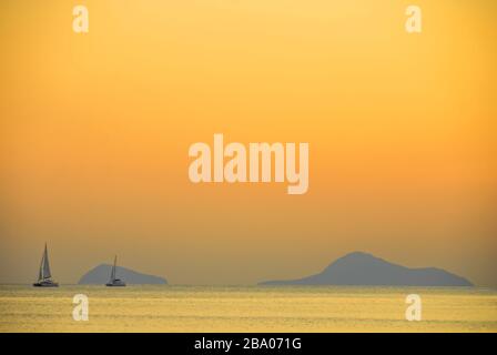 Segelboot in der Ferne unter der untergehenden Sonne in der Nähe von Santorini, Griechenland Stockfoto