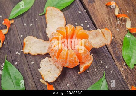Orange radial geschält wie eine Blume auf Holzhintergrund. Tangentiale Früchte teilweise geschält gereinigt Stockfoto